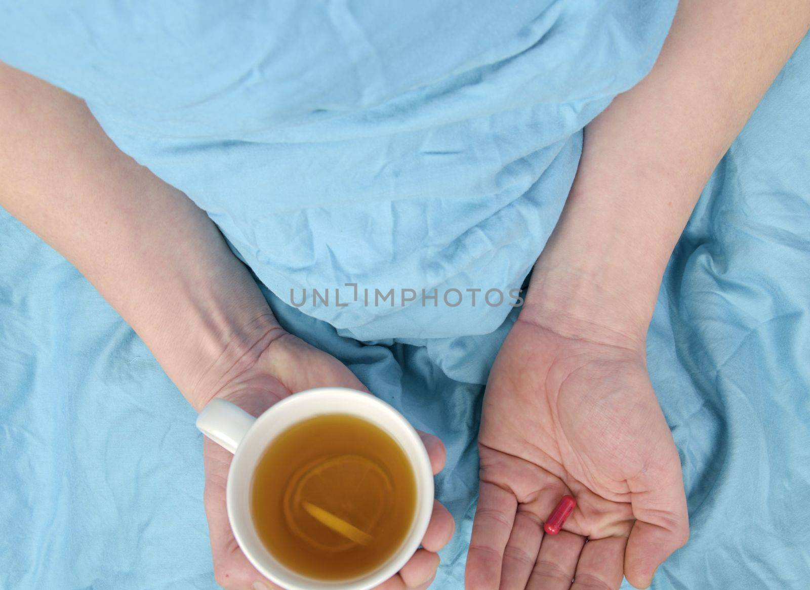 Ill man with fever drinking cup of warm tea and taking pill. Influenza season. Hands of the sick man holding pill and cup of the hot tea in the bed. Close-up of ill caucasian man at home.