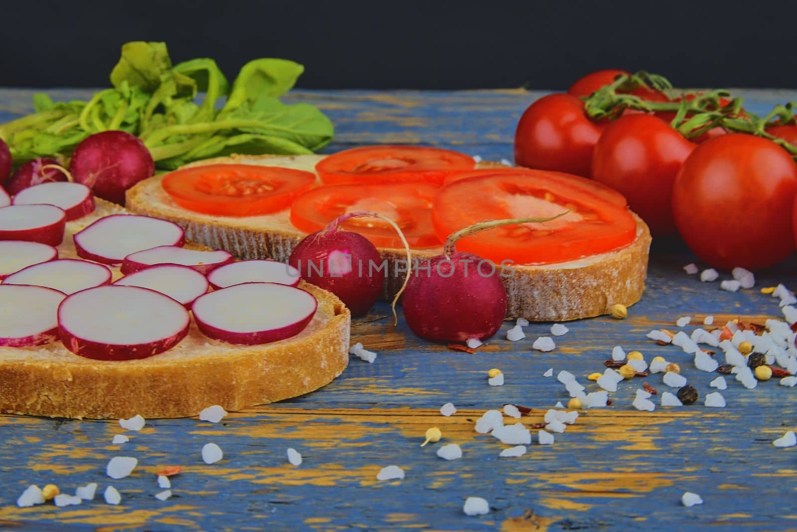 Spread butter on bread with sliced tomatoes and radishes. Fresh snack on natural wooden background by roman_nerud