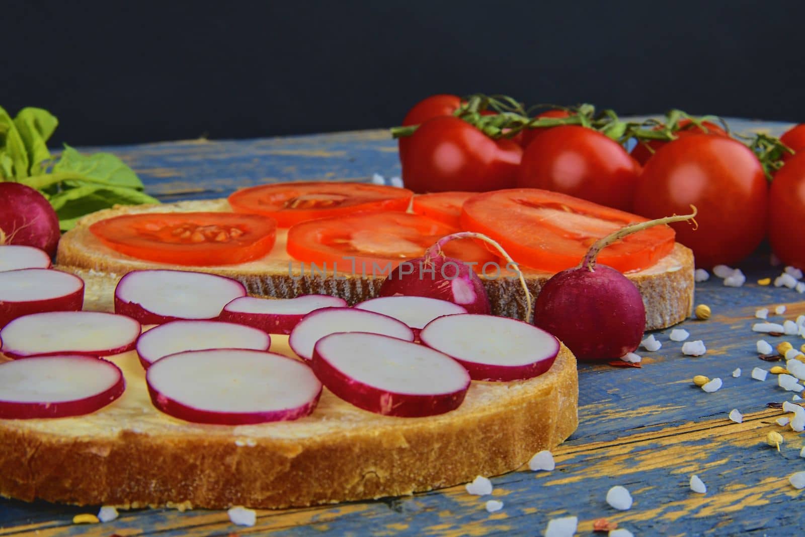 Spread butter on bread with sliced tomatoes and radishes. Fresh snack on natural wooden background.