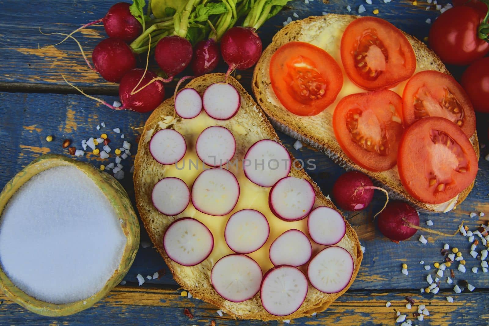 Spread butter on bread with sliced tomatoes and radishes. Fresh snack on natural wooden background. Flat design. Top view by roman_nerud