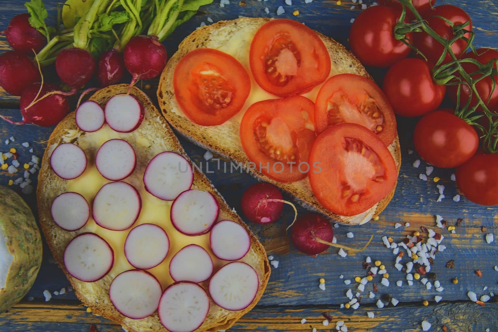 Spread butter on bread with sliced tomatoes and radishes. Fresh snack on natural wooden background. Flat design. Top view.