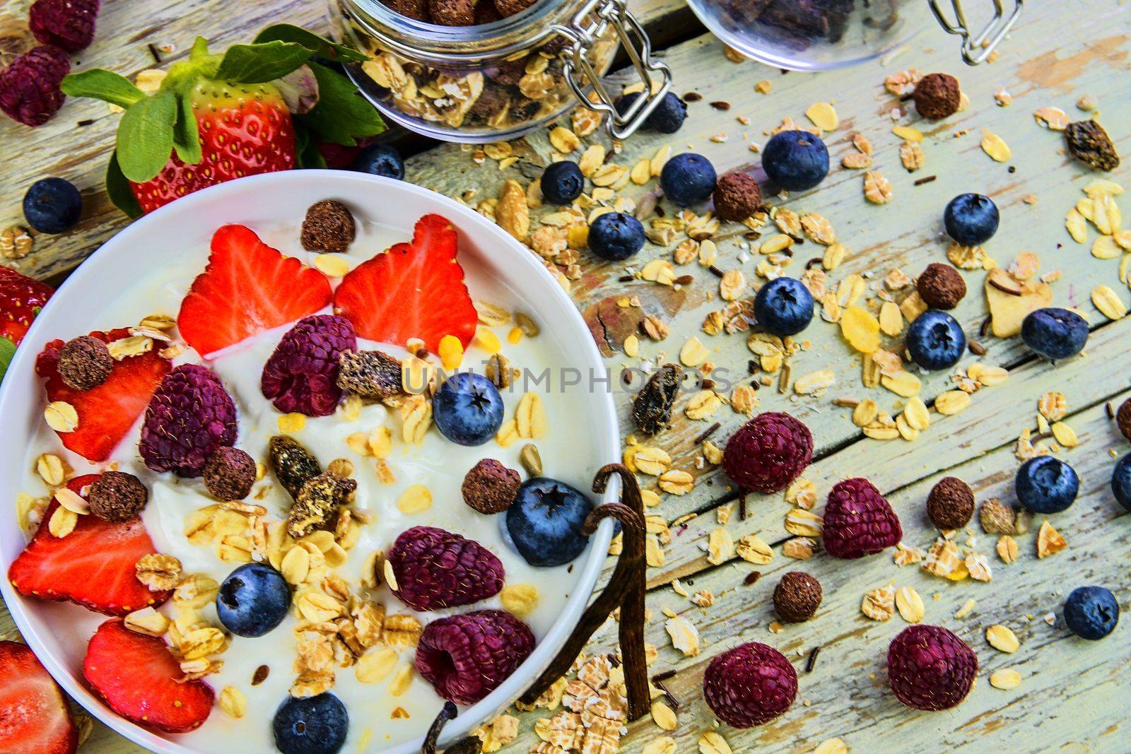 Healthy breakfast, cereal with yoghurt, strawberries, blueberries, raspberries and muesli on wooden rustic background.  Concept of: fitness, diet, wellness and breakfasts.