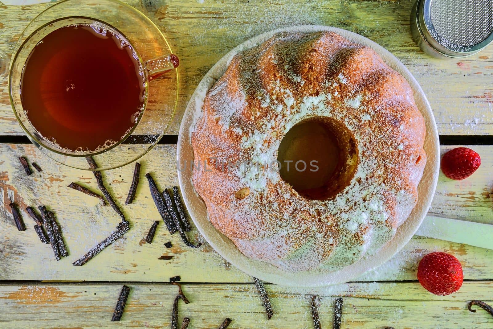 Old fashioned sand cake with cup of black tea and pieces of vanilla on wooden background. Egg-yolk sponge cake with stawberries on rustic white background. Top view. Flat design.