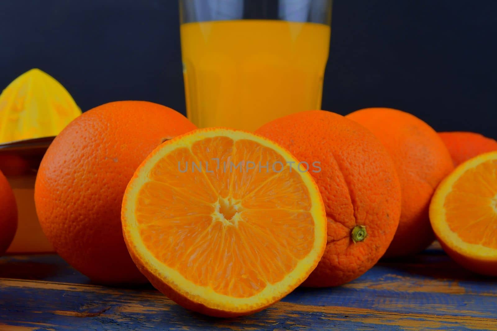 Tangerines, oranges, a glass of orange juice and manual citrus squezeer on blue wooden background. Oranges cut in half by roman_nerud