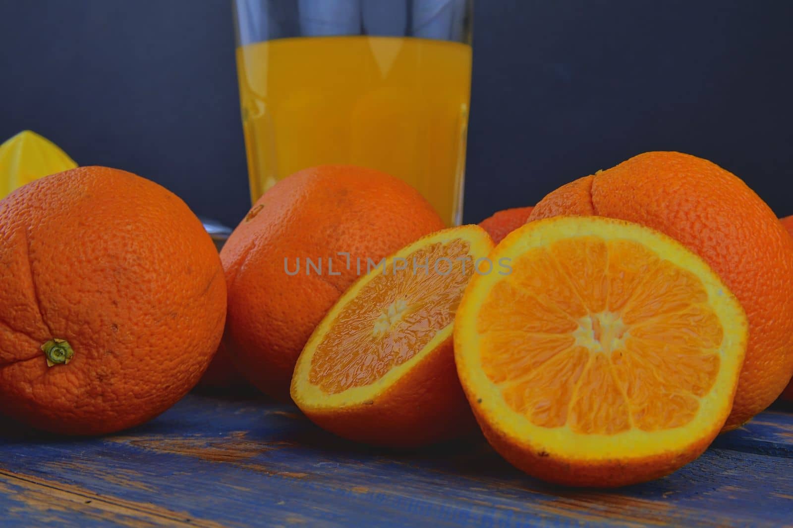 Tangerines, oranges, a glass of orange juice and manual citrus squezeer on blue wooden background. Oranges cut in half by roman_nerud