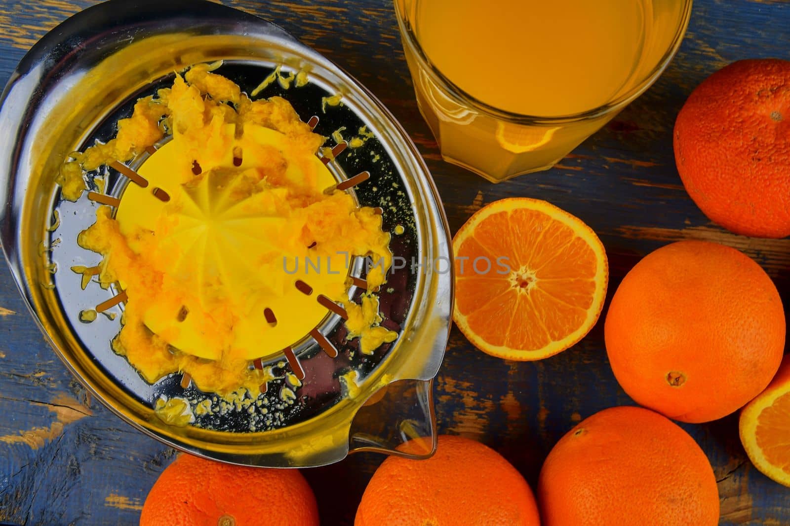Tangerines, oranges, a glass of orange juice and manual citrus squezeer on blue wooden background. Oranges cut in half. Top view, flat design.