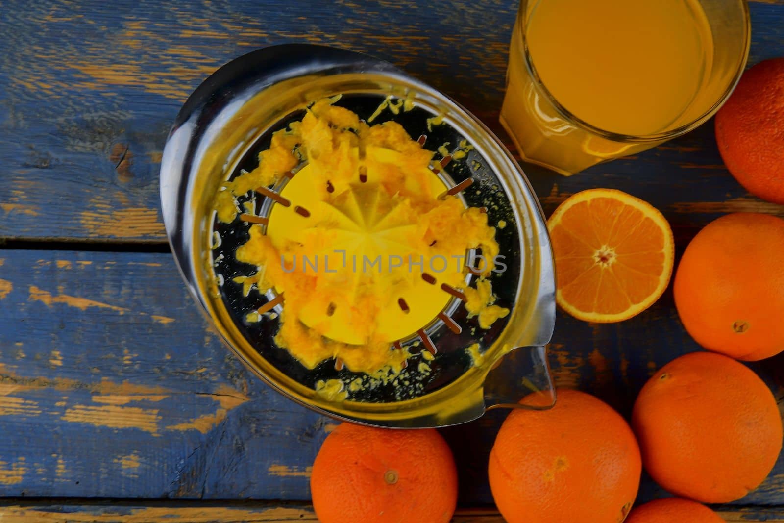 Tangerines, oranges, a glass of orange juice and manual citrus squezeer on blue wooden background. Oranges cut in half. Top view, flat design by roman_nerud