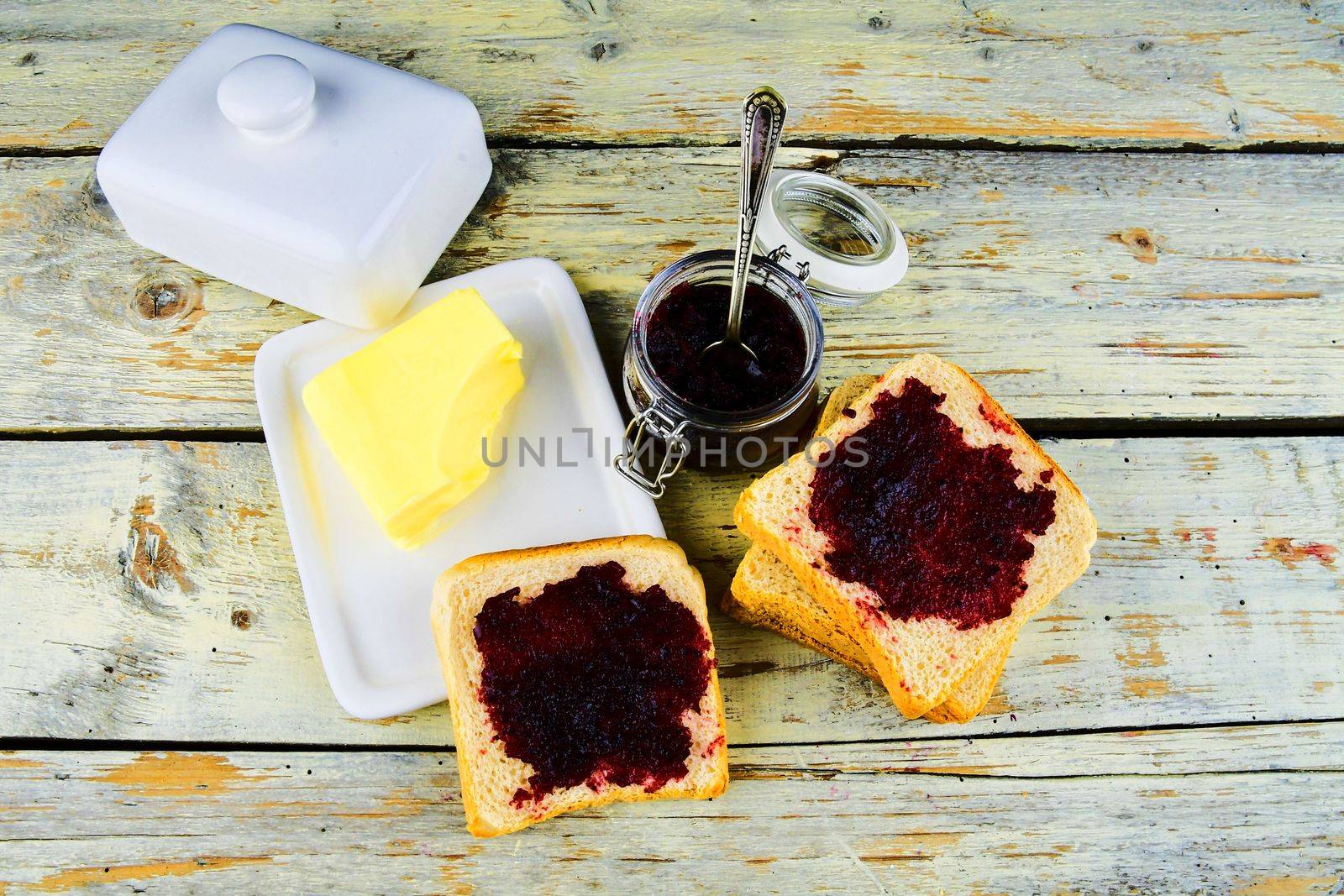 Jam, butter in butter dish and jam spread on toast. Healthy and diet concept. Rural white wooden background. Flat design, top view.