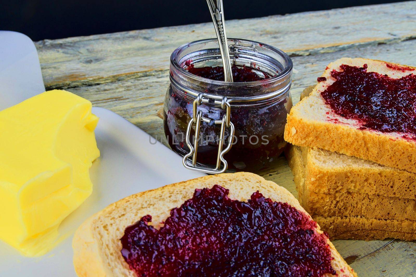 Jam, butter in butter dish and jam spread on toast. Healthy and diet concept. Rural white wooden background.