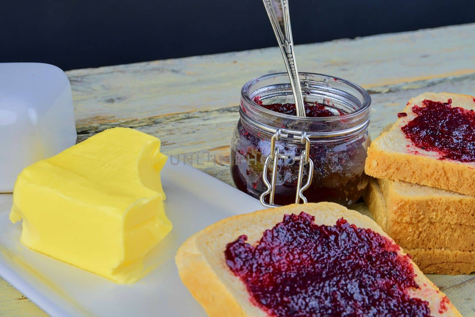 Jam, butter in butter dish and jam spread on toast.  Healthy and diet concept. Rural white wooden background.  by roman_nerud