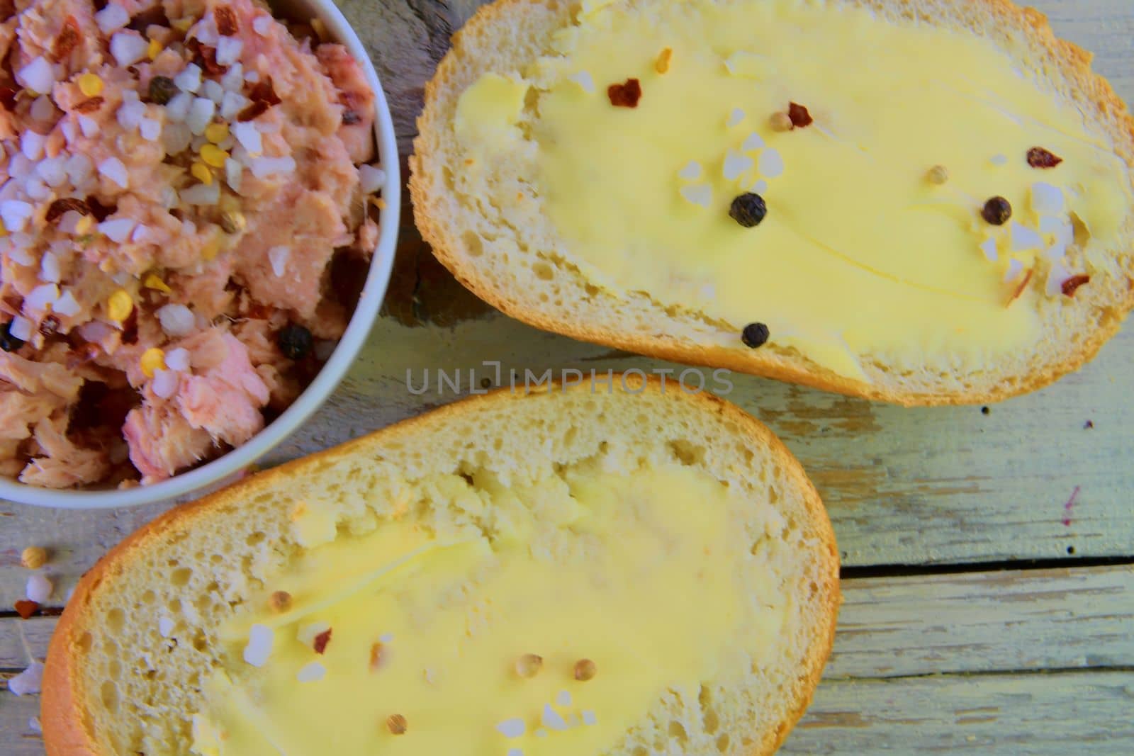 Slices of baguettes with butter and  fresh tuna with spices on wooden background. Top view. Flat design. 