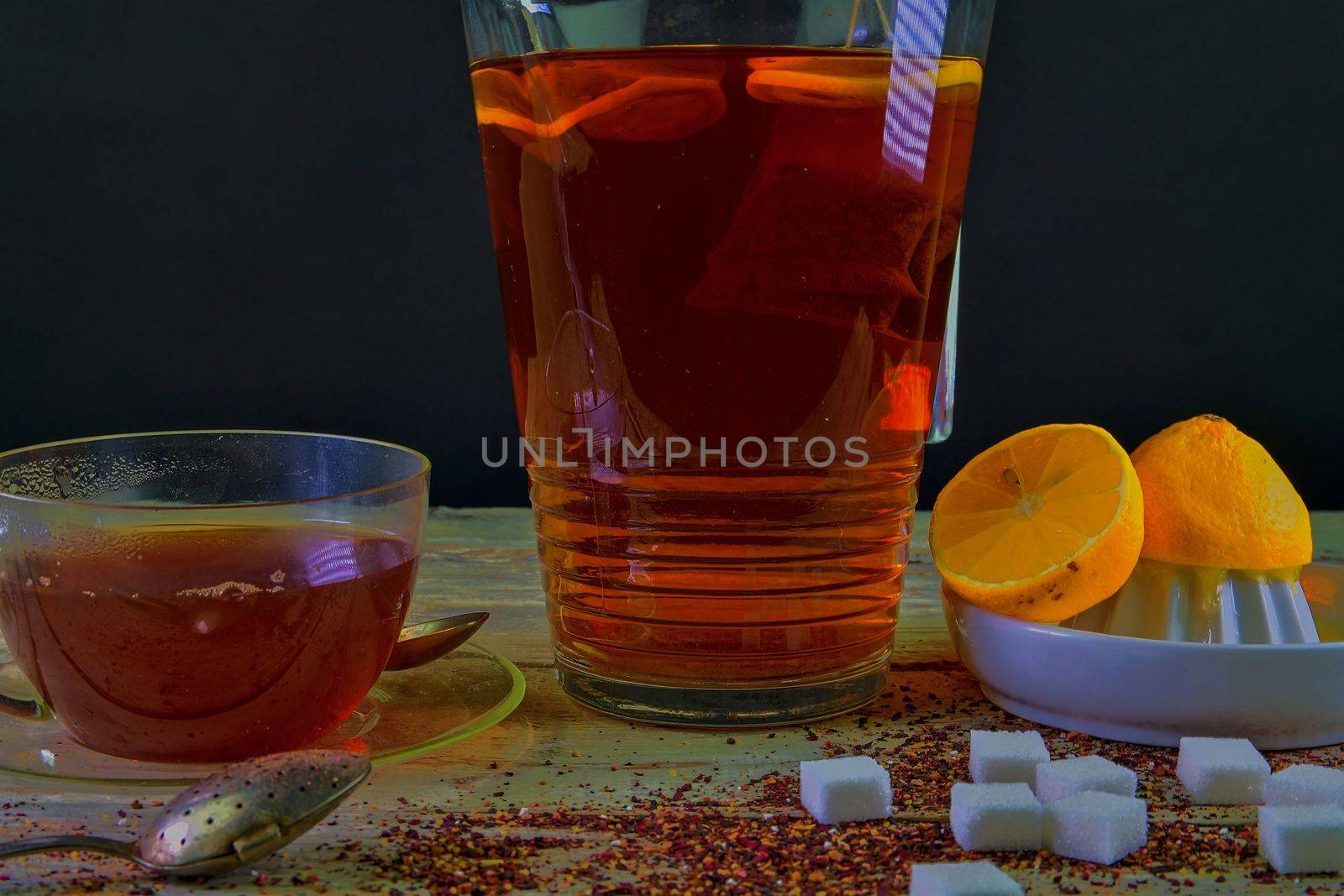 Black tea, a cup of black tea, manual squeezer with lemons. A jug of black tea and cubes of sugar. Dark image. 