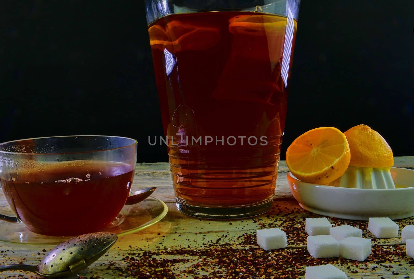 Black tea, a cup of black tea, manual squeezer with lemons. A jug of black tea and cubes of sugar. Dark image. 