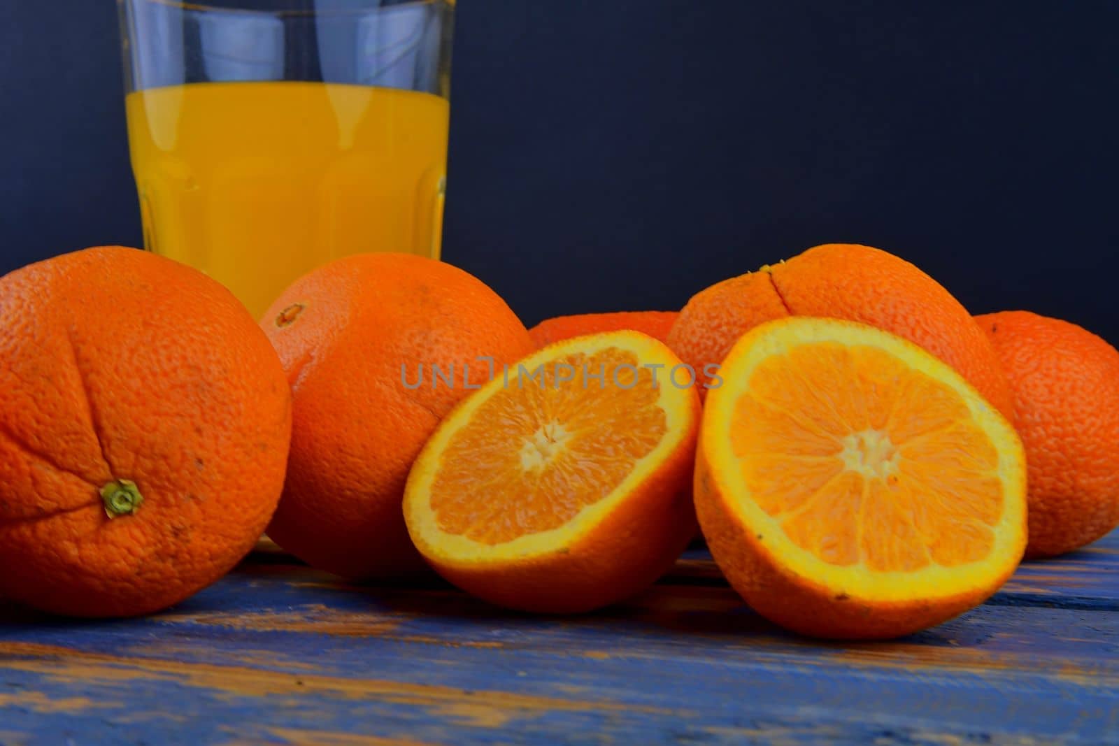 Tangerines, oranges, a glass of orange juice and manual citrus squezeer on blue wooden background. Oranges cut in half. Close-up by roman_nerud