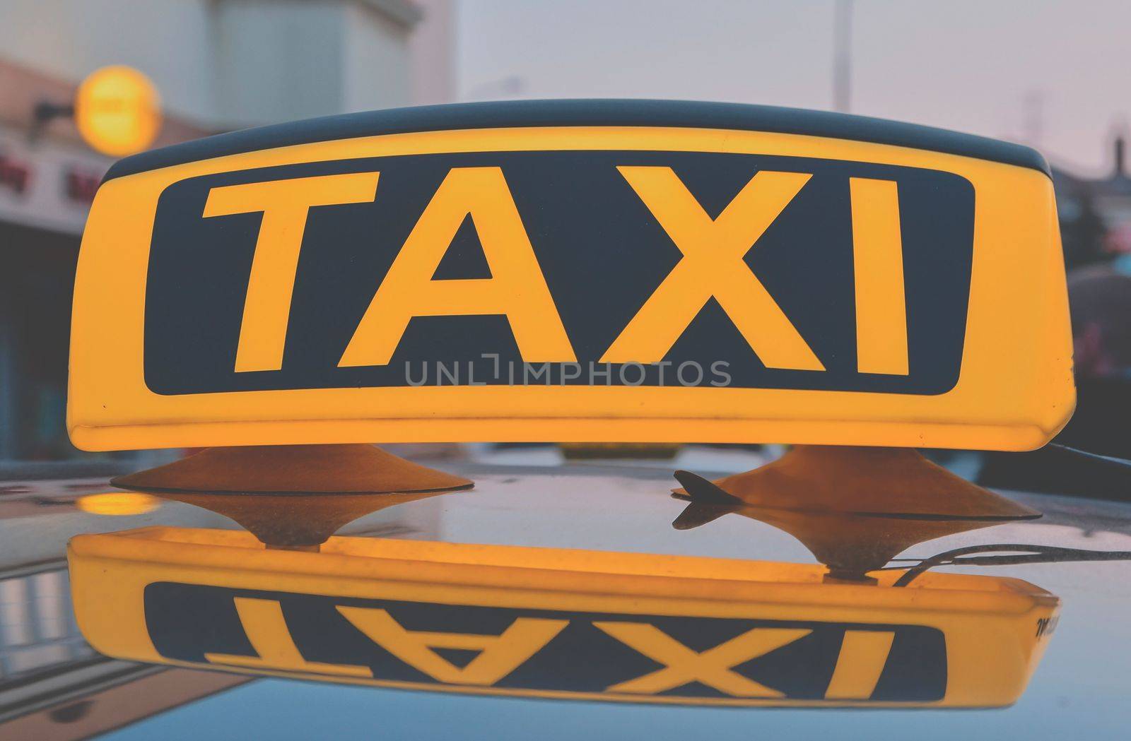 Lit taxi sign on roof of taxi car in the city.
