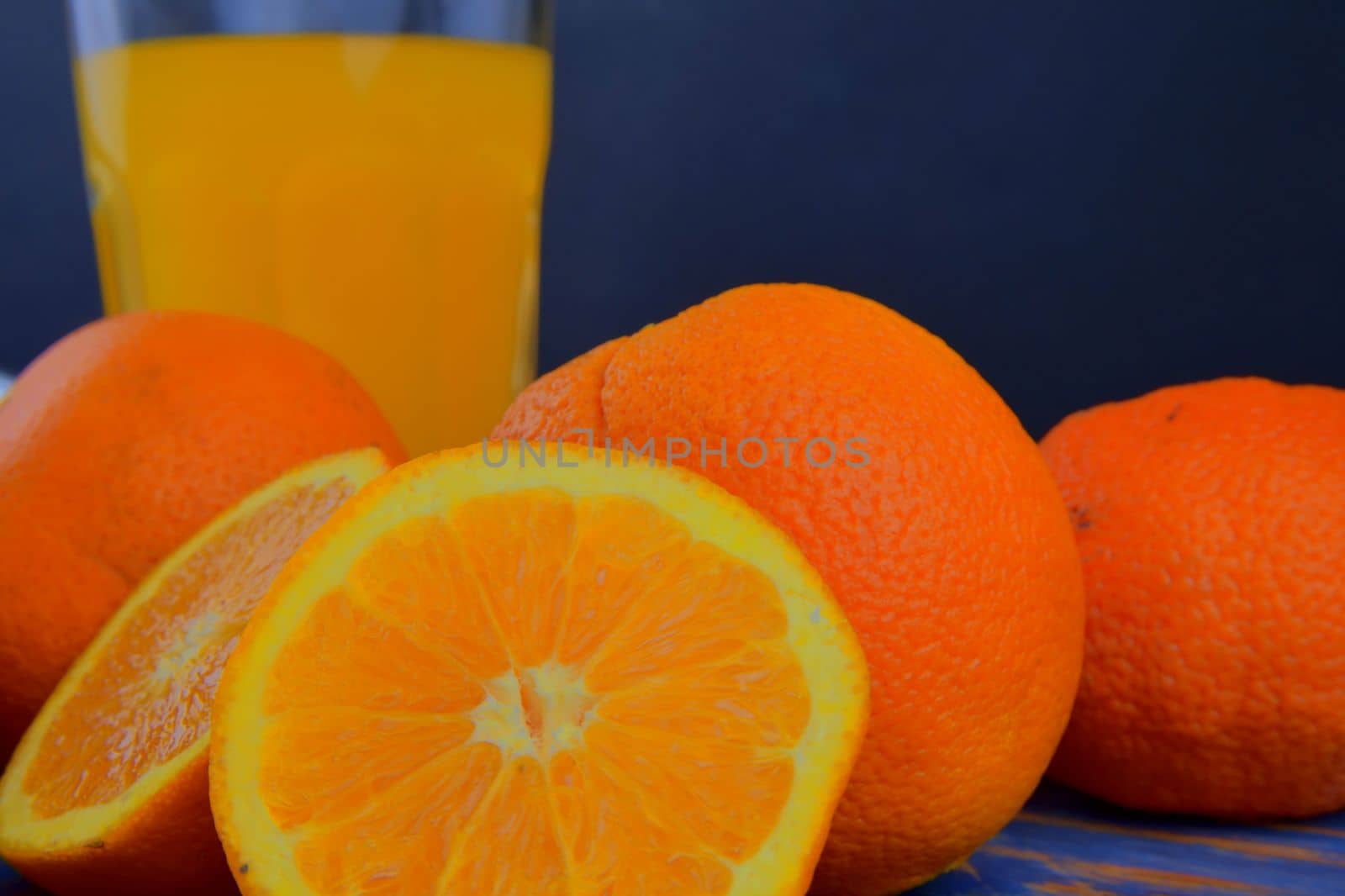 Tangerines, oranges, a glass of orange juice and manual citrus squezeer on blue wooden background. Oranges cut in half. Close-up. 