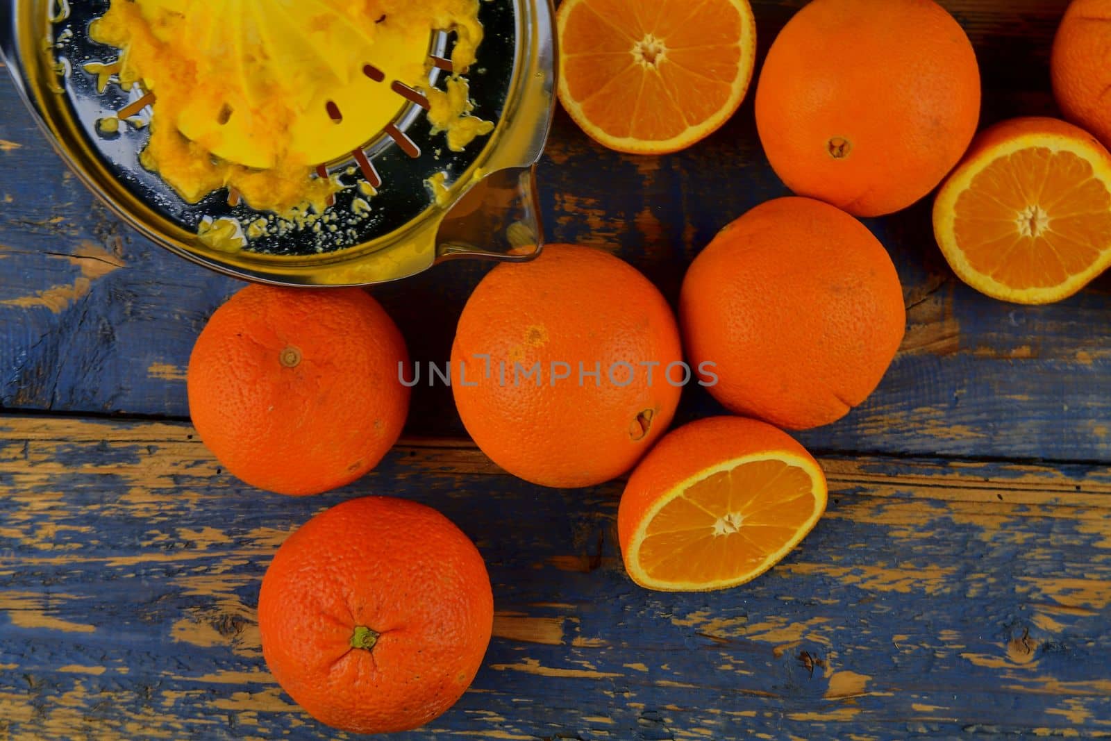 Tangerines, oranges, a glass of orange juice and manual citrus squezeer on blue wooden background. Oranges cut in half. Top view, flat design by roman_nerud