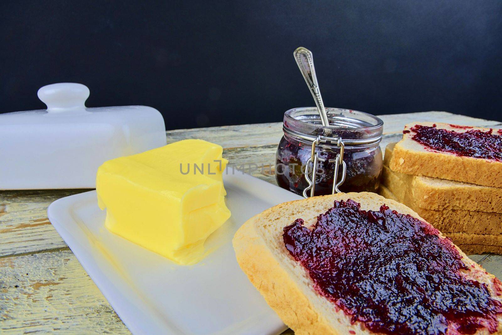 Jam, butter in butter dish and jam spread on toast. Healthy and diet concept. Rural white wooden background.