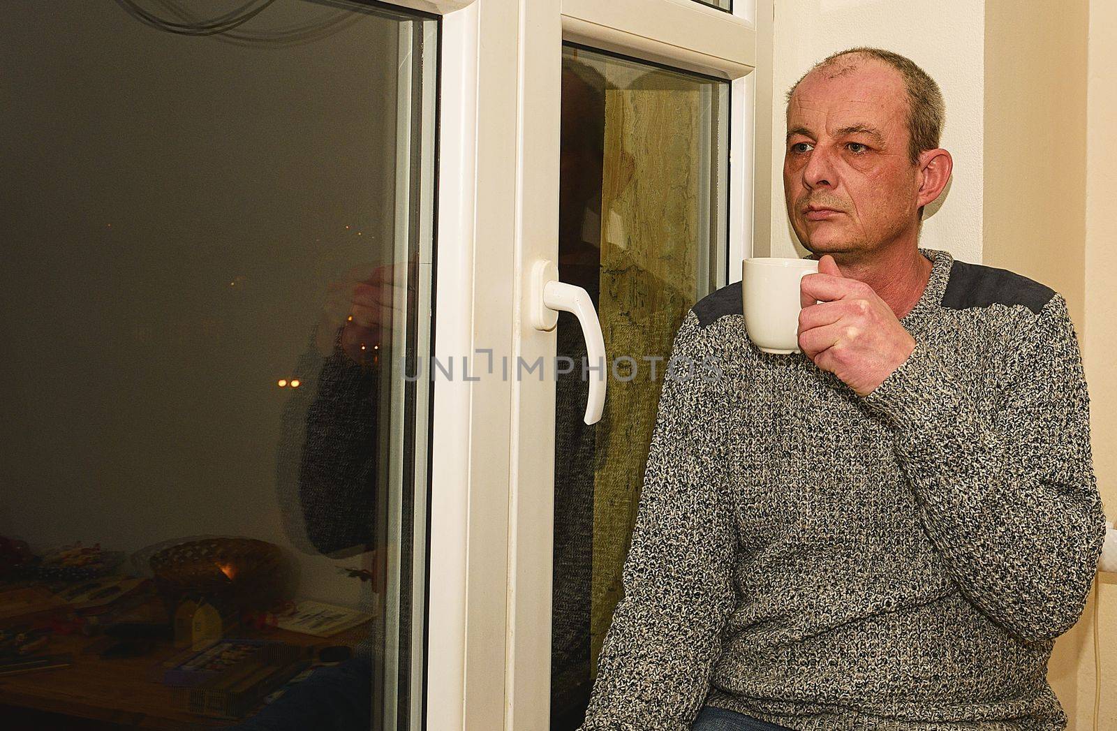 Depressed middle age man sitting near window. Sad man drinking coffee. 
