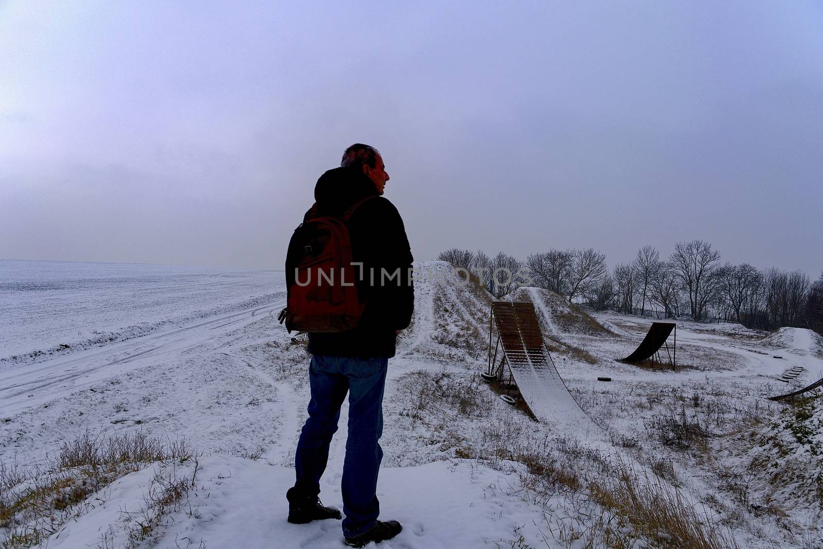 Man viewing on abandoned freestyle motocross ramps. Middle age man standing in winter landscape during sunsrise.