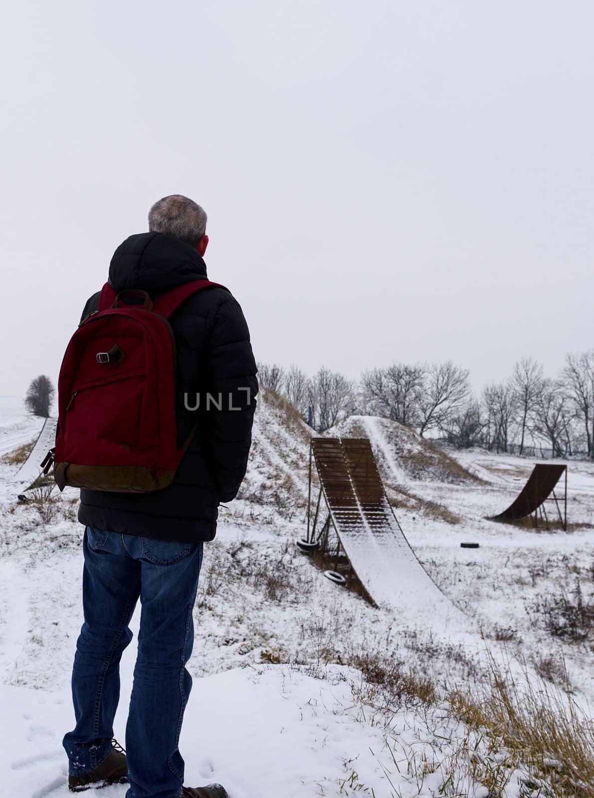 Middle age man standing in beautiful winter landscape . Man viewing on abandoned freestyle motocross ramps.