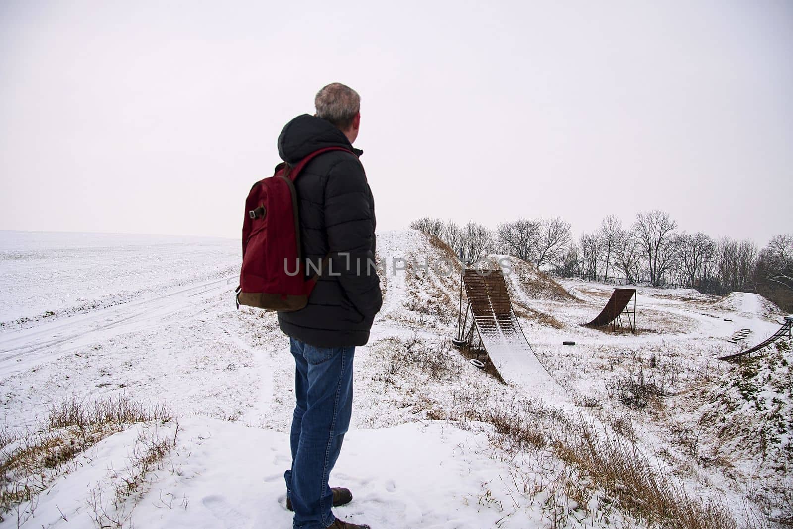 Middle age man standing in beautiful winter landscape . Man viewing on abandoned freestyle motocross ramps by roman_nerud