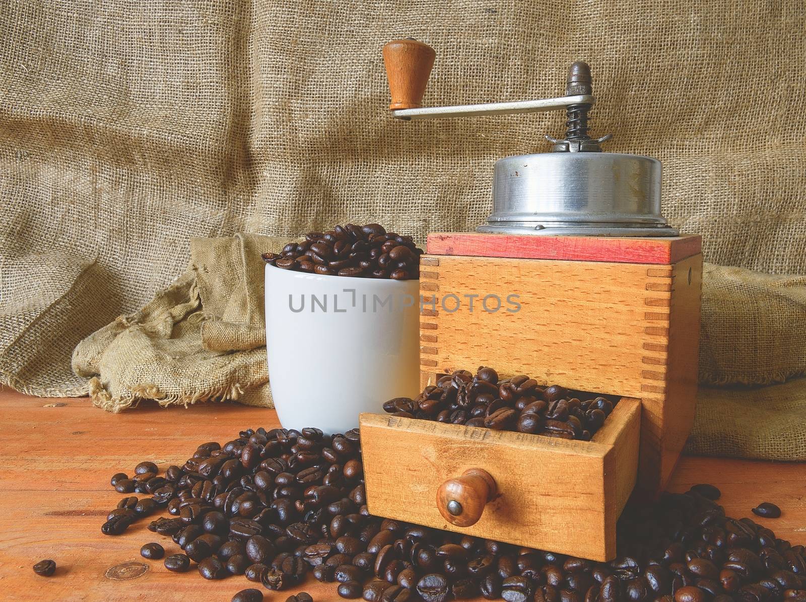 Vintage coffee mill, coffee beans and white cup filled coffee beans on wooden background. 