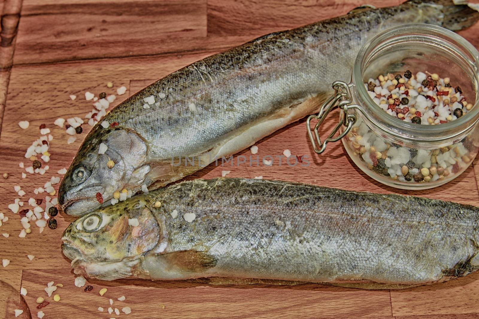 Two raw rainbow trouts with spices on wooden board. Healthy food and dieting concept. Add dark contrasts. Close-up by roman_nerud