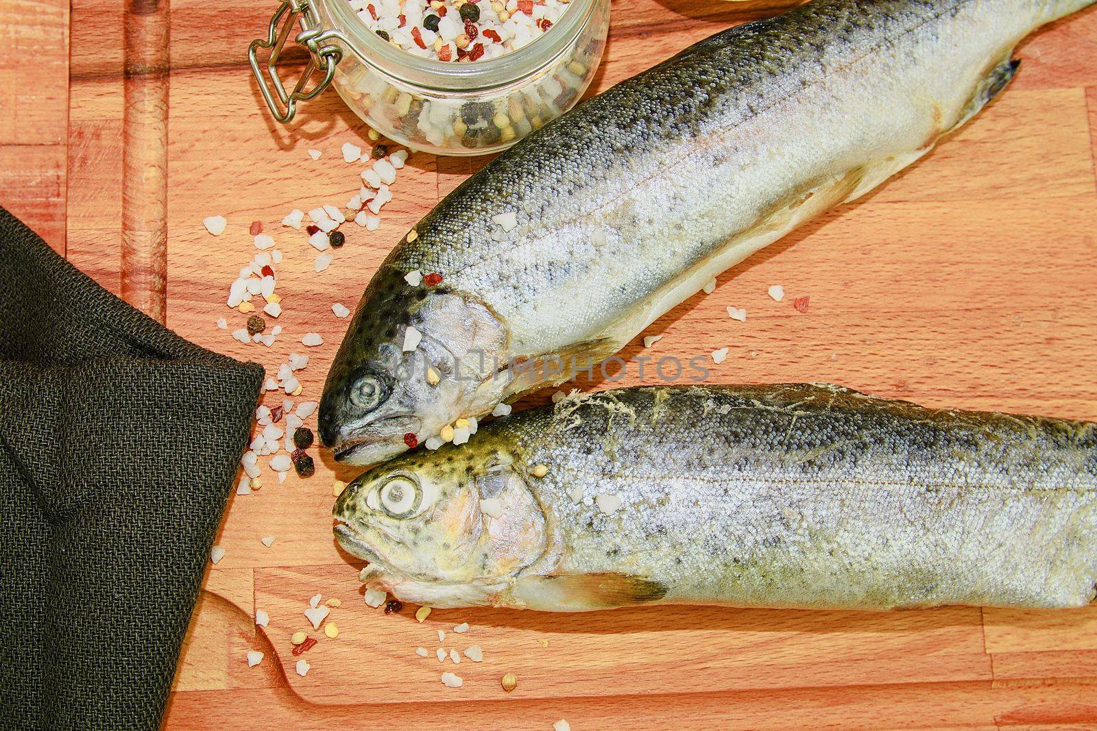 Two raw rainbow trouts with spices on wooden board. Healthy food and dieting concept. Close-up.