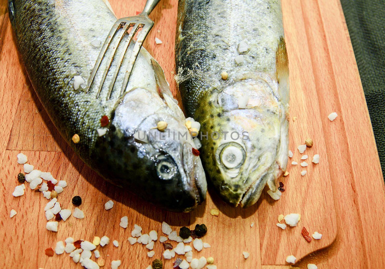 Fresh raw rainbow trouts with spices and fork on wooden board. Healthy food and dieting concept. Close-up.