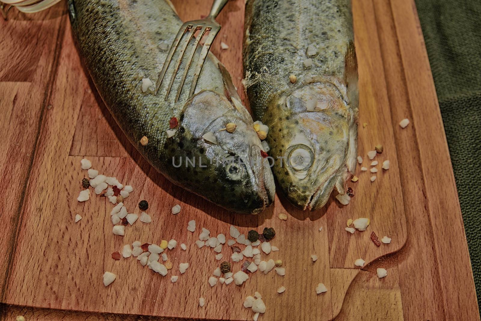 Fresh raw rainbow trouts with spices and fork on wooden board. Healthy food and dieting concept. Close-up. Add dark contrasts by roman_nerud