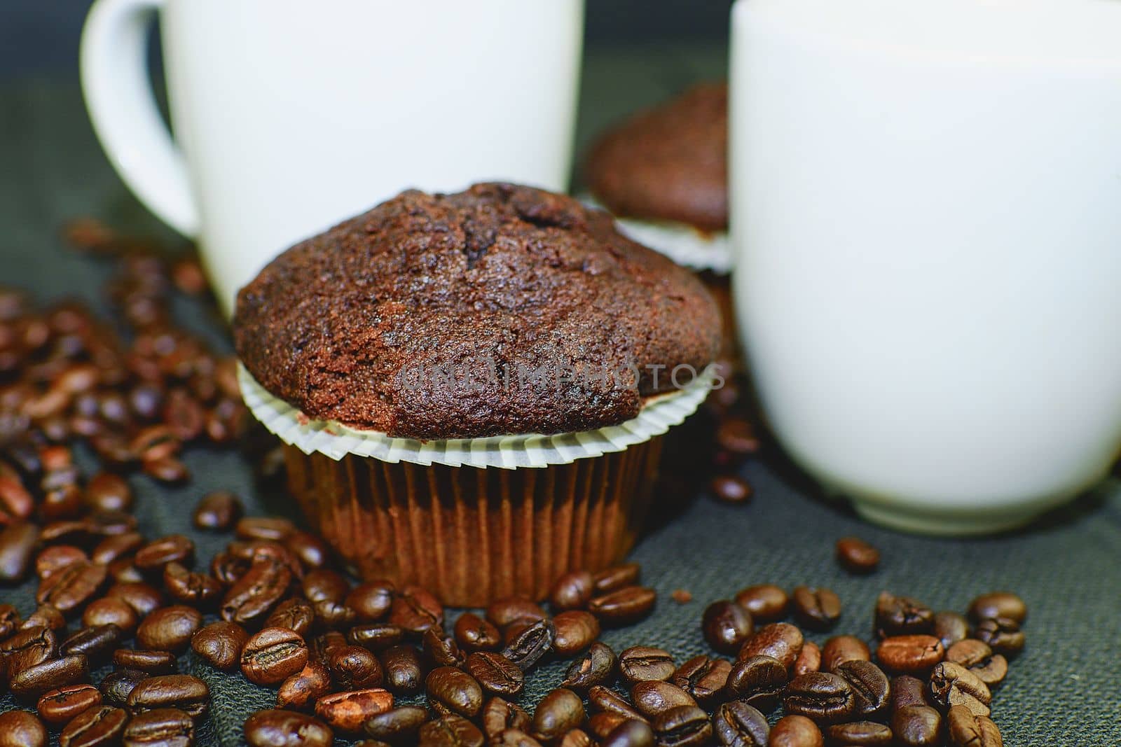 Dark muffins, cups of coffee and coffee beans on black background