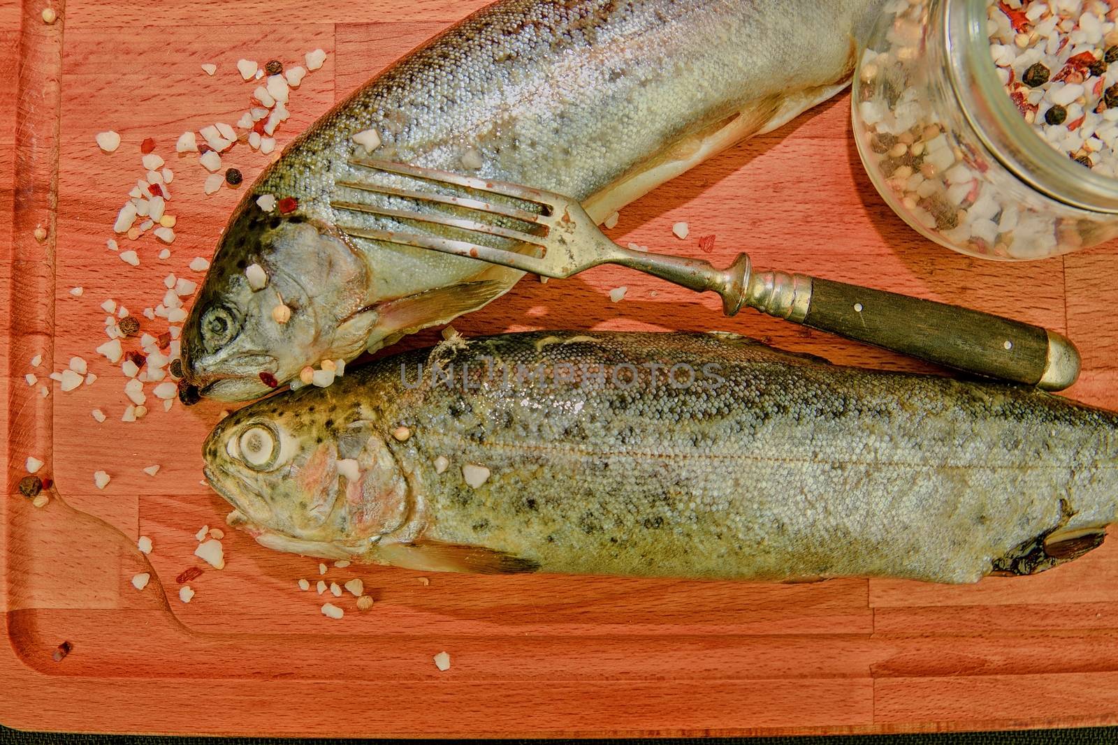 Fresh raw rainbow trouts with spices and fork on wooden board. Healthy food and dieting concept. Close-up. Add soft dark contrasts by roman_nerud
