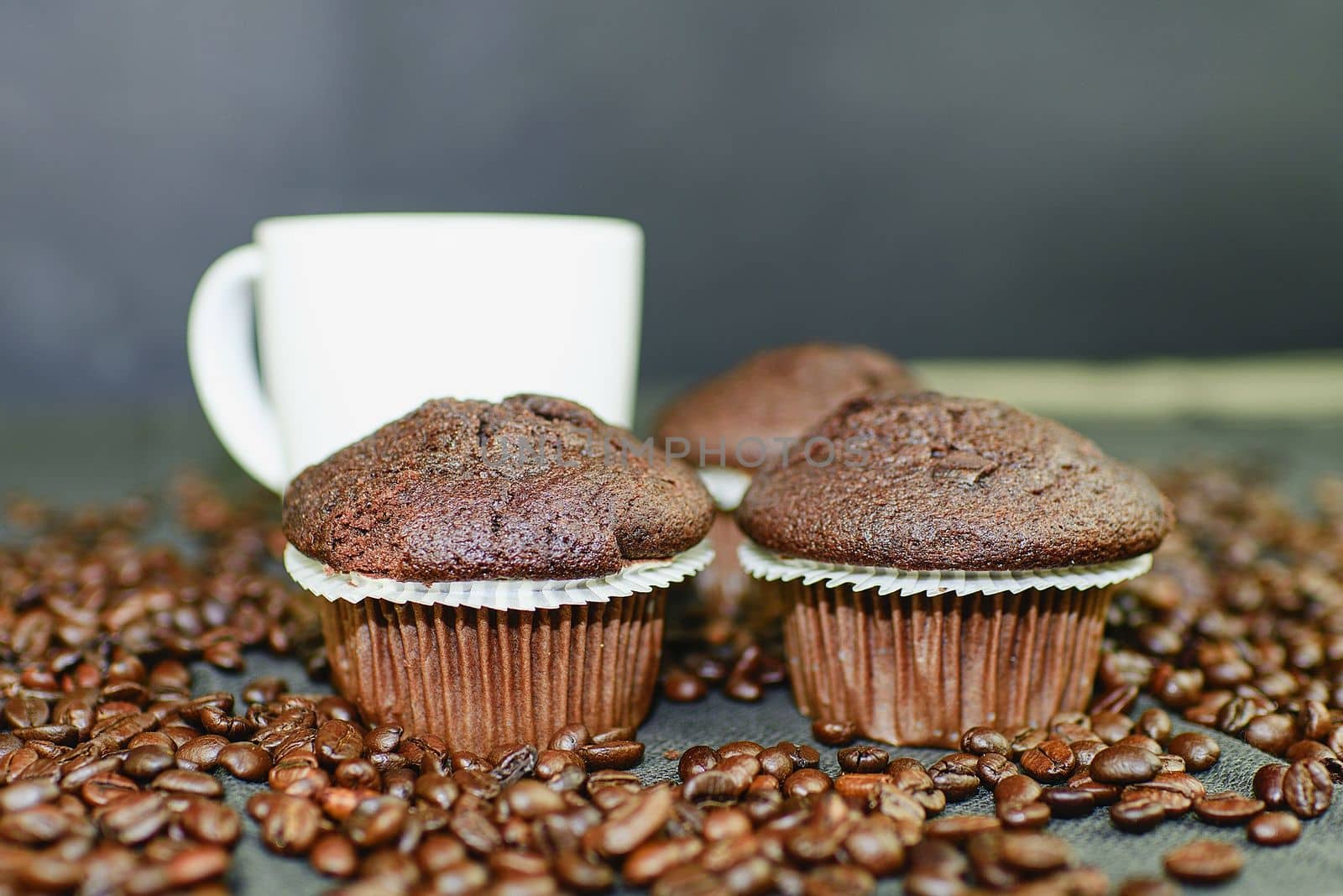 Dark muffins, cups of coffee and coffee beans on black background. Black copy space. Coffee bar concept.