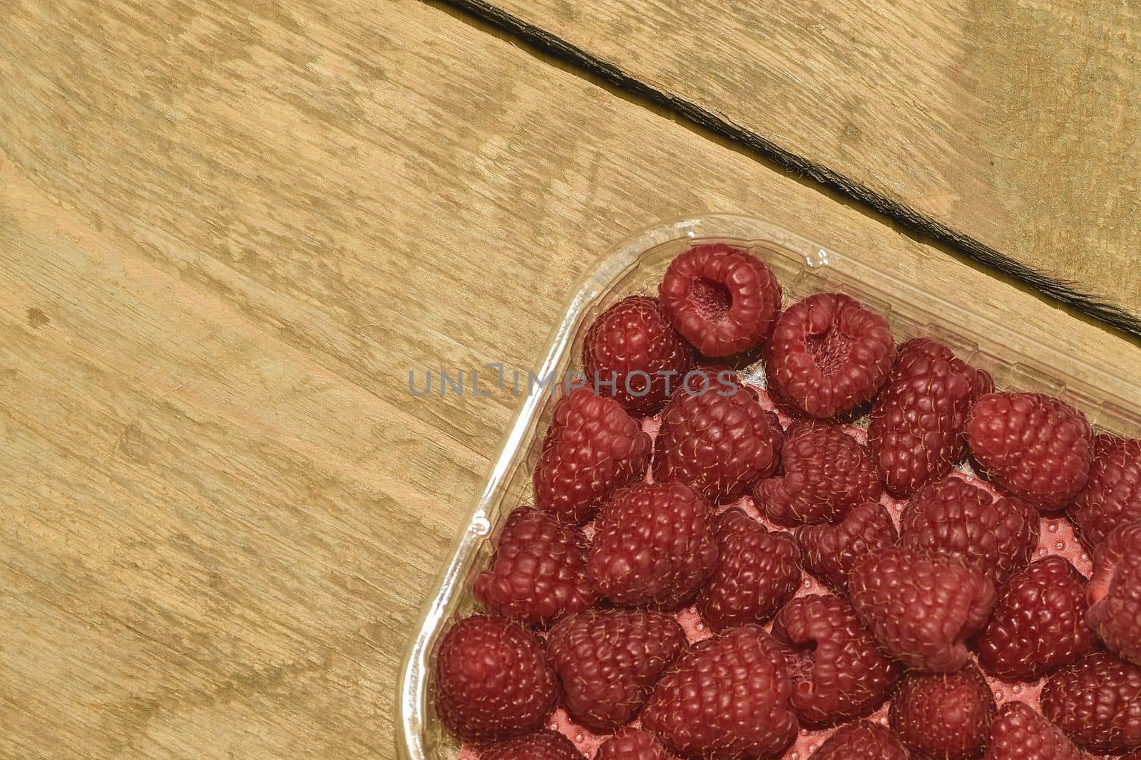 Red-fruited raspberries in plastic box on wooden background. Raspberries background. Close-up.