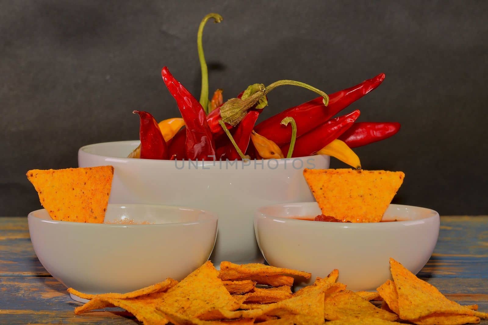 Chili corn-chips with salsa dip and chili peppers on wooden background. 
