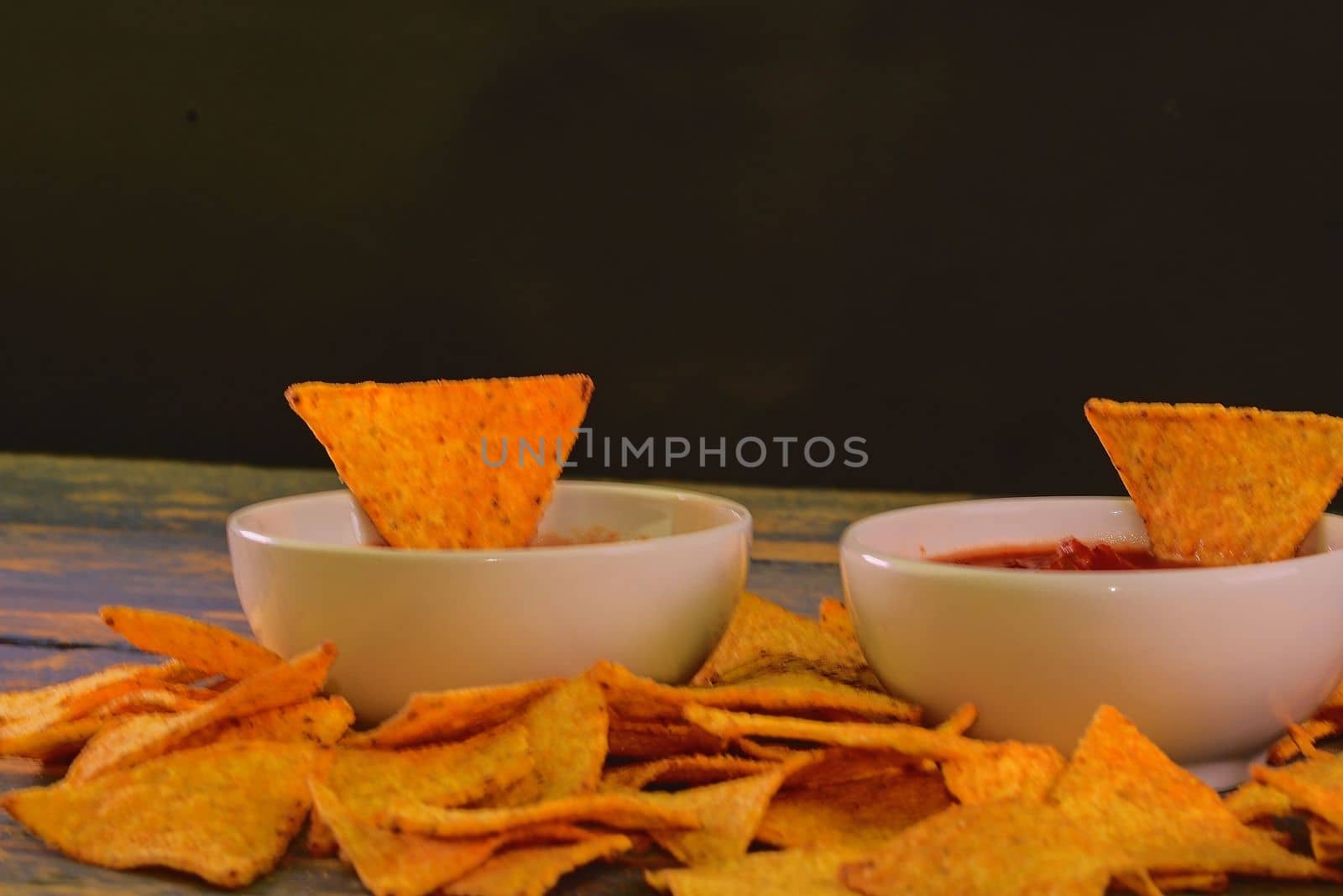 Chili corn-chips with salsa dip on wooden background. Black copy space for text.