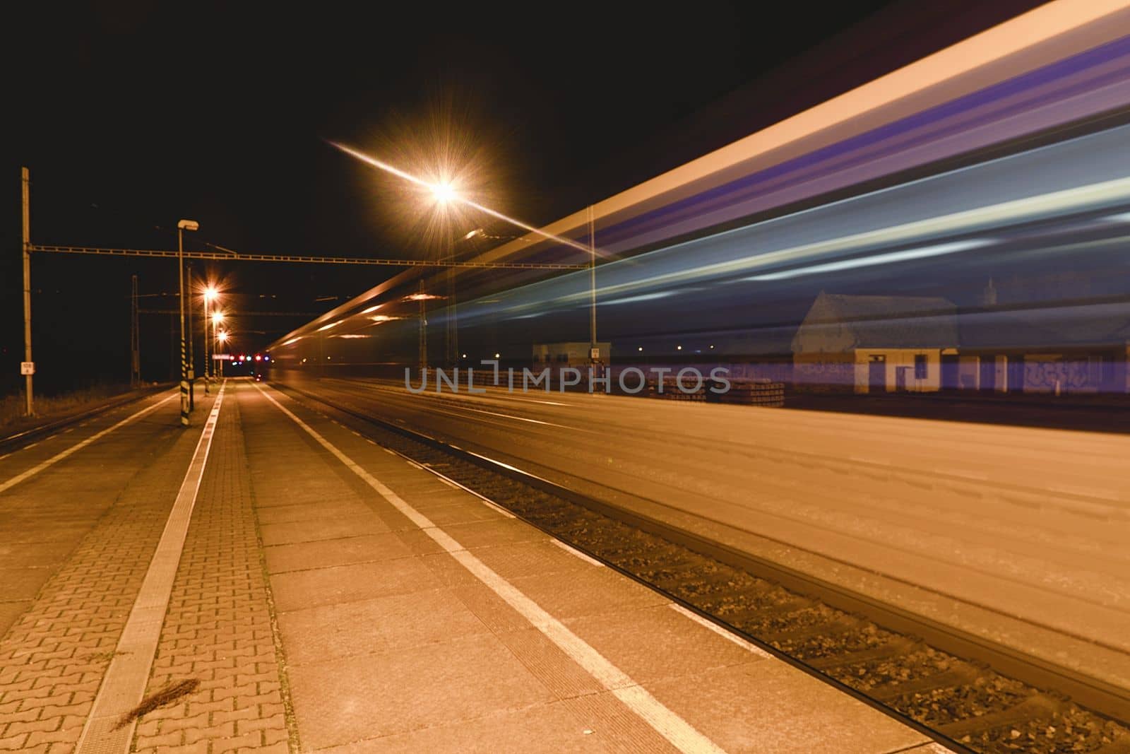Light trail of the express train in the railway station at the night. Railway platform a the night by roman_nerud
