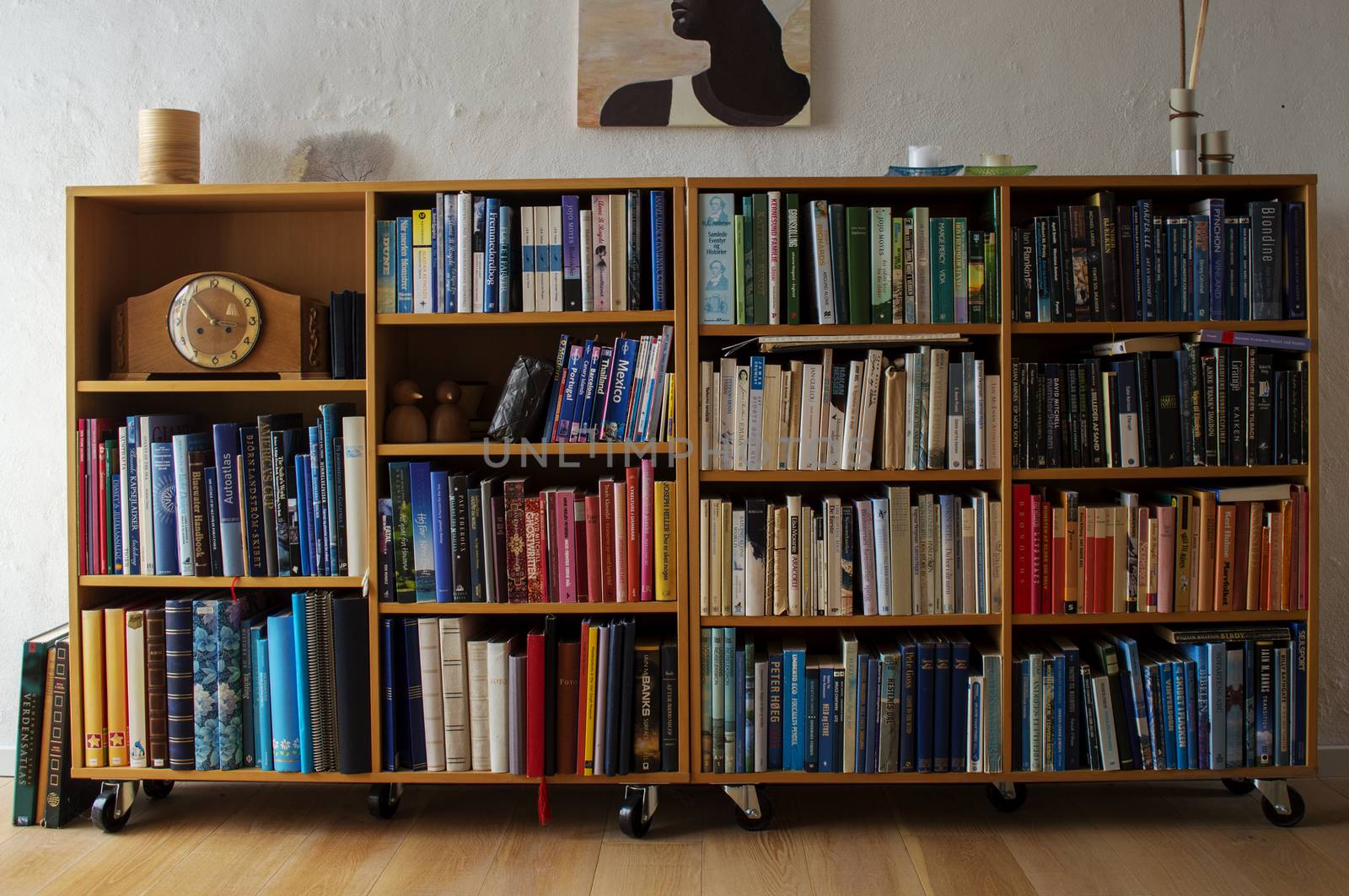 Wooden book shelf with many colorful books and a clock.
