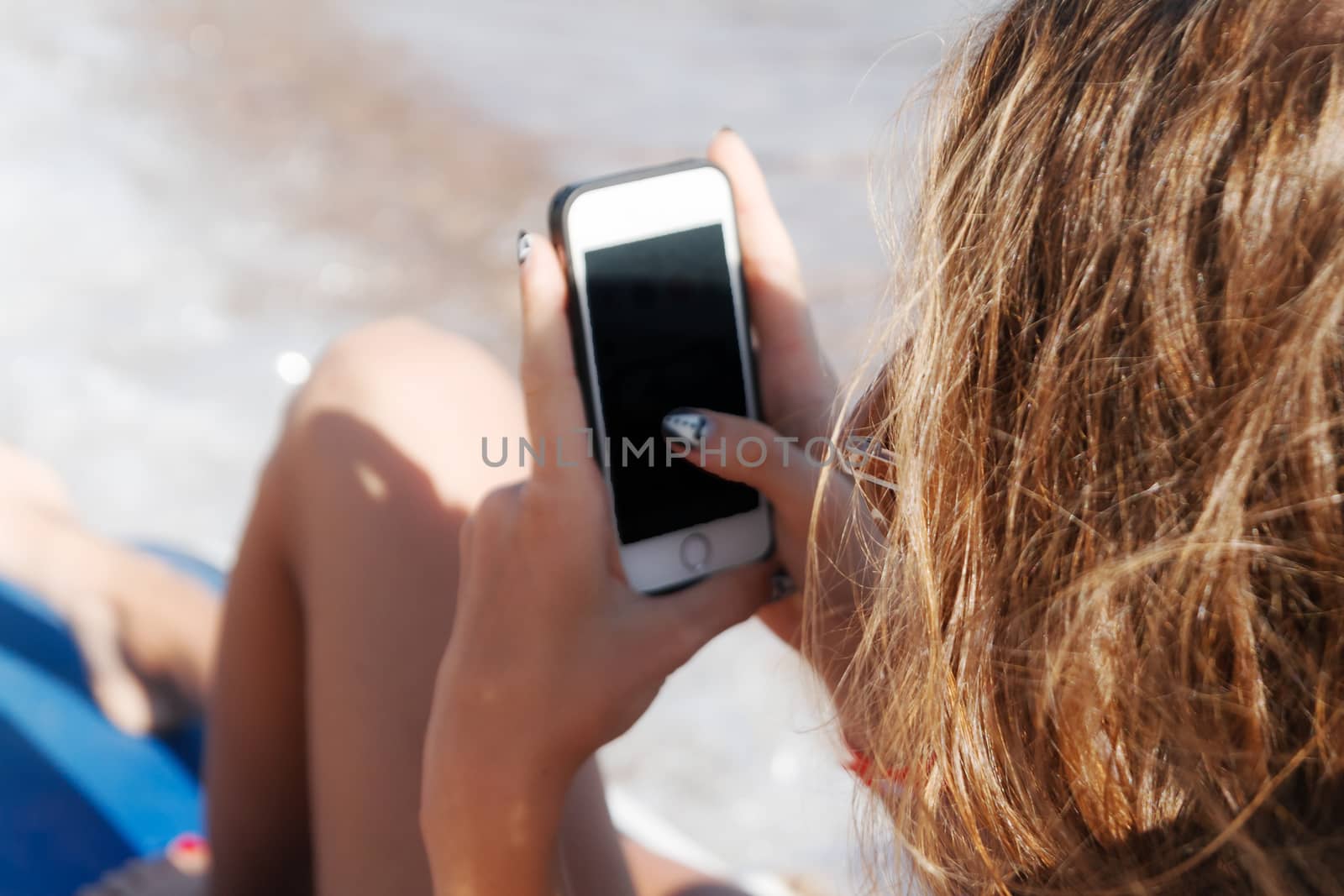 A young tanned woman looks into a smartphone through sunglasses on a lounger. The concept of a lifestyle is always on the Internet.