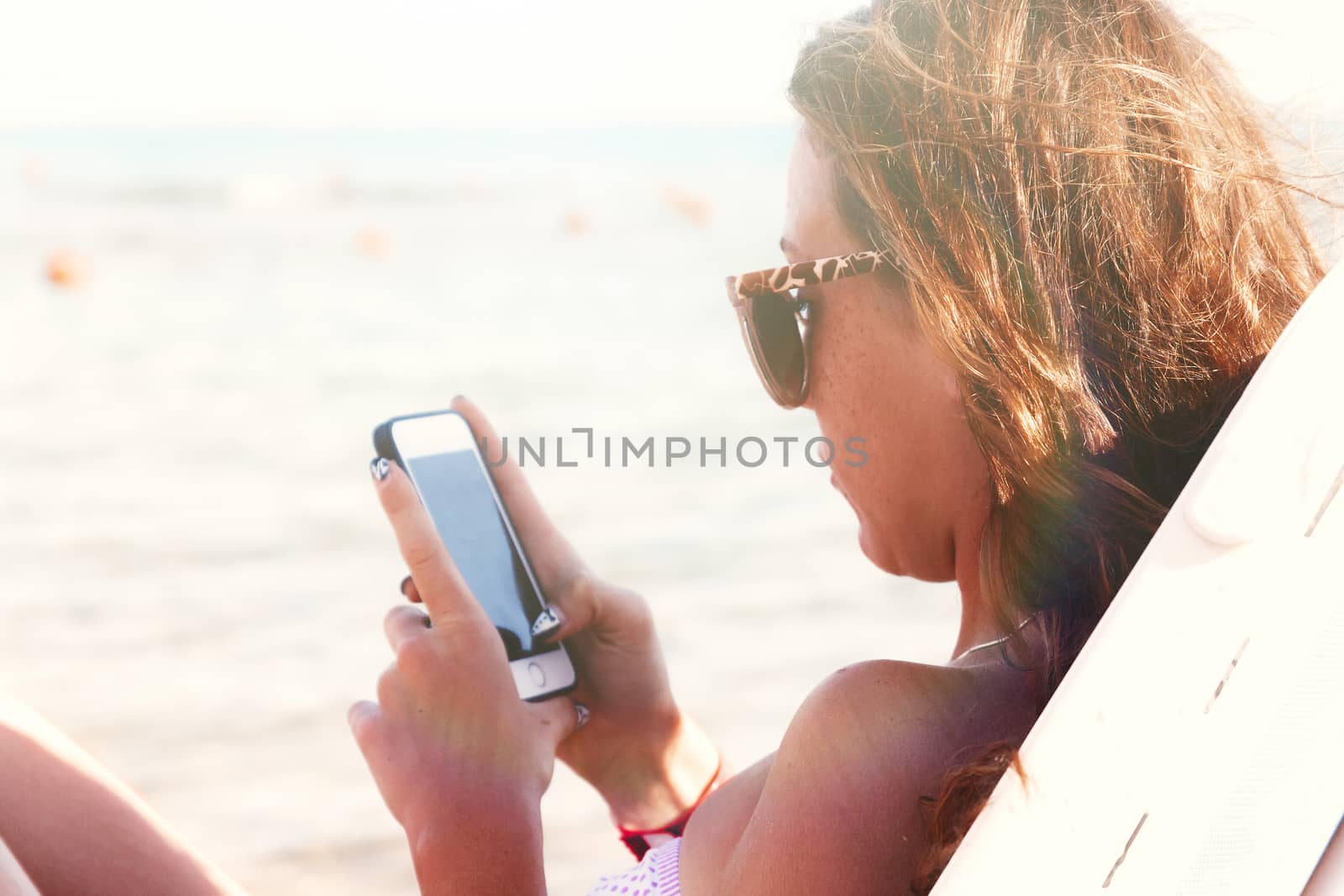A young tanned woman looks into a smartphone through sunglasses  by Tanacha