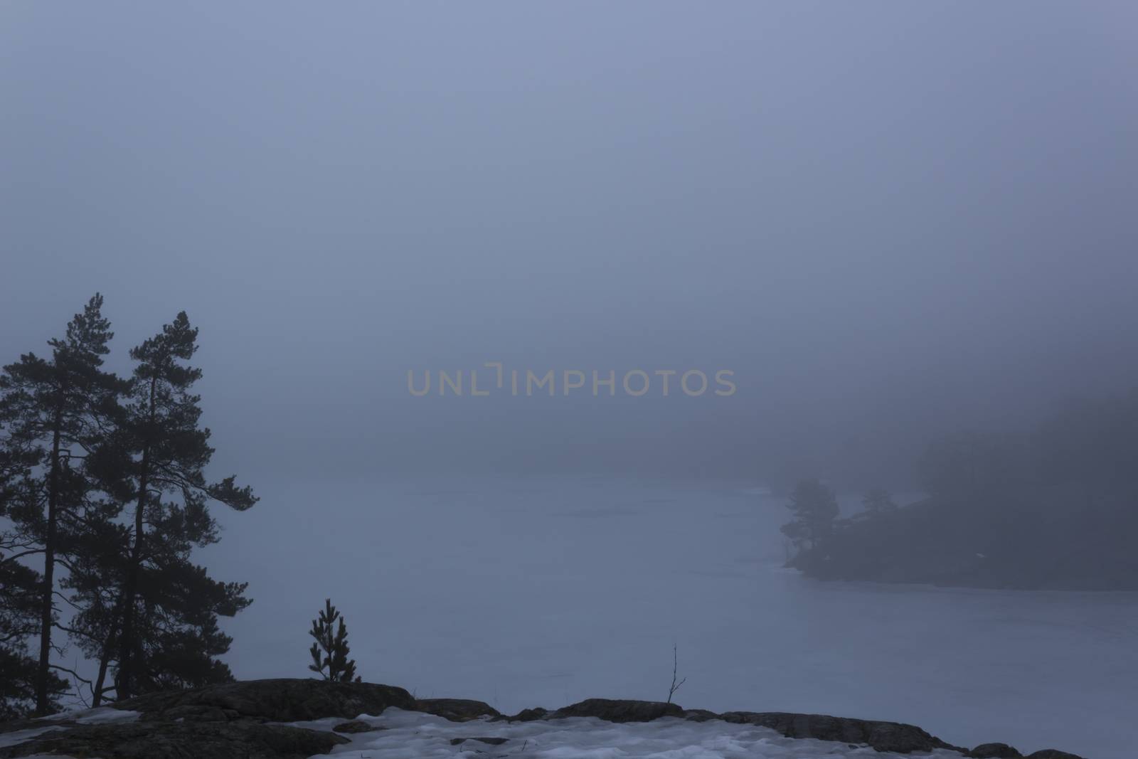 Frozen lake surrounded by mountains with pine and fir trees on a misty, moody, day. Nackareservatet - nature reserve in Sweden