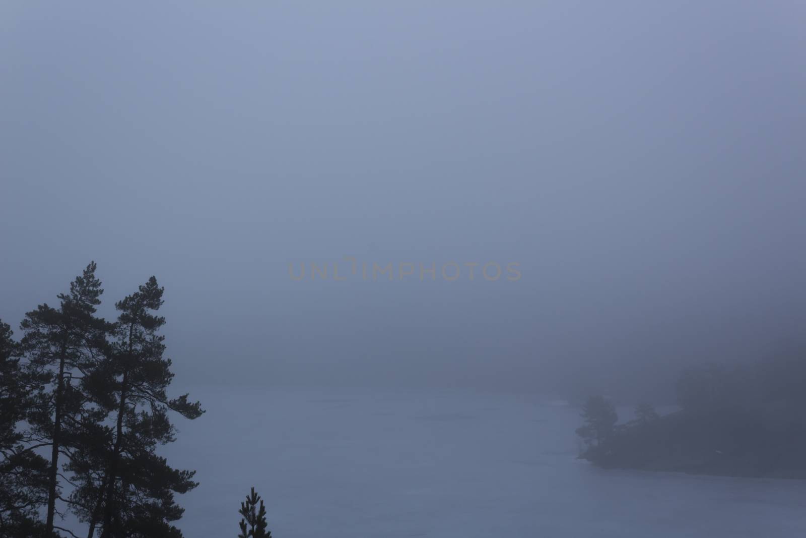 Frozen lake surrounded by mountains with pine and fir trees on a misty, moody, day. Nackareservatet - nature reserve in Sweden