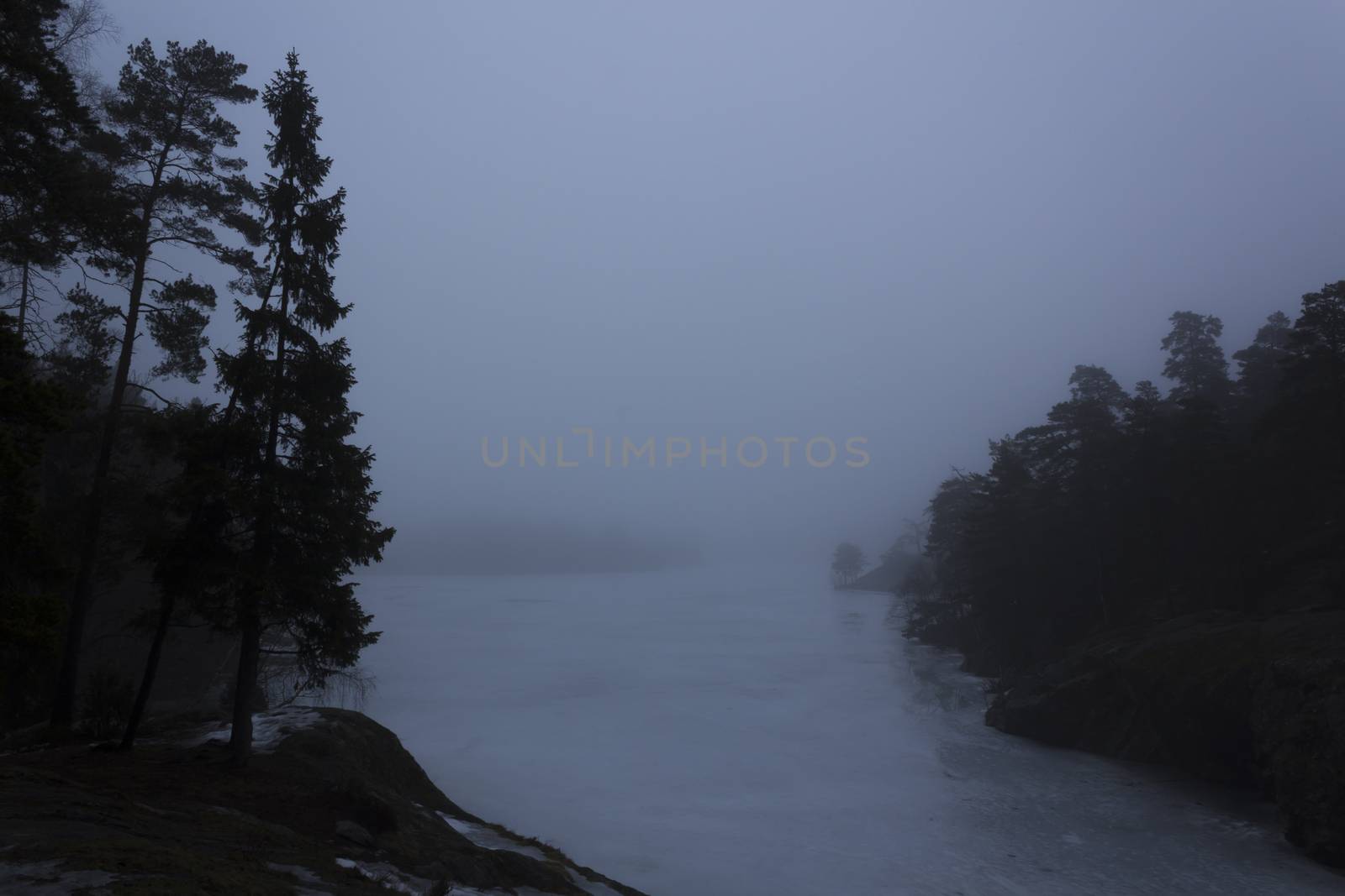 Frozen lake surrounded by small mountains with pine and fir trees on a misty, moody, day. Nackareservatet - nature reserve in Sweden