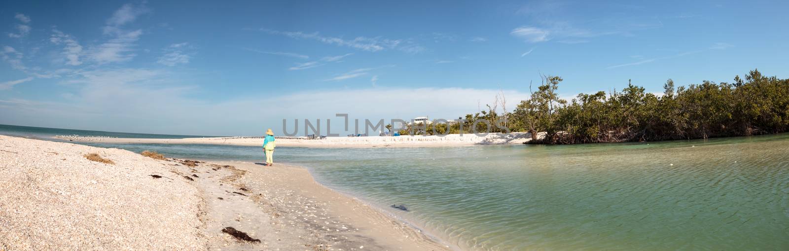 Older woman stands on the white sand beach in front of aqua blue water of Clam Pass in Naples, Florida in the morning.