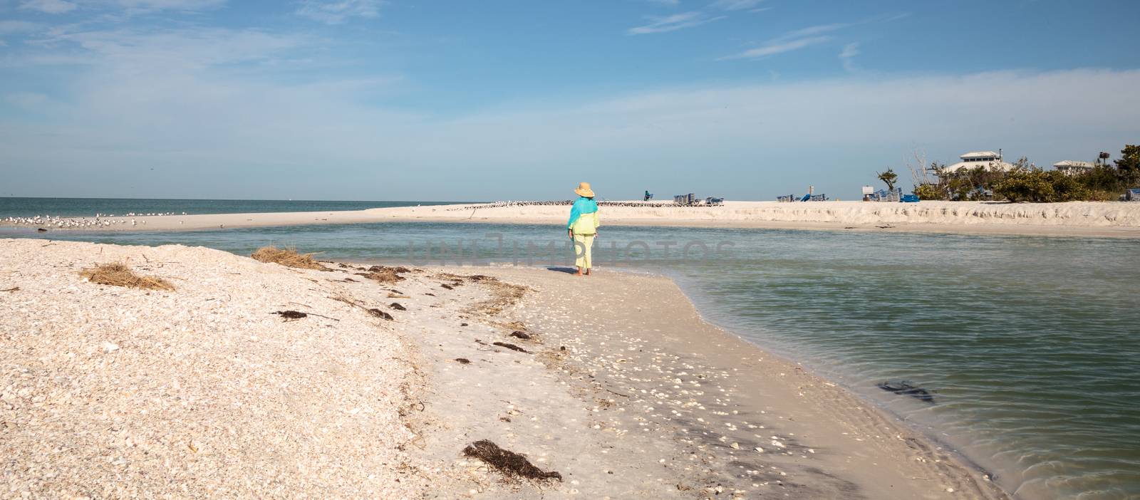 Older woman stands on the white sand beach in front of aqua blue water of Clam Pass in Naples, Florida in the morning. 