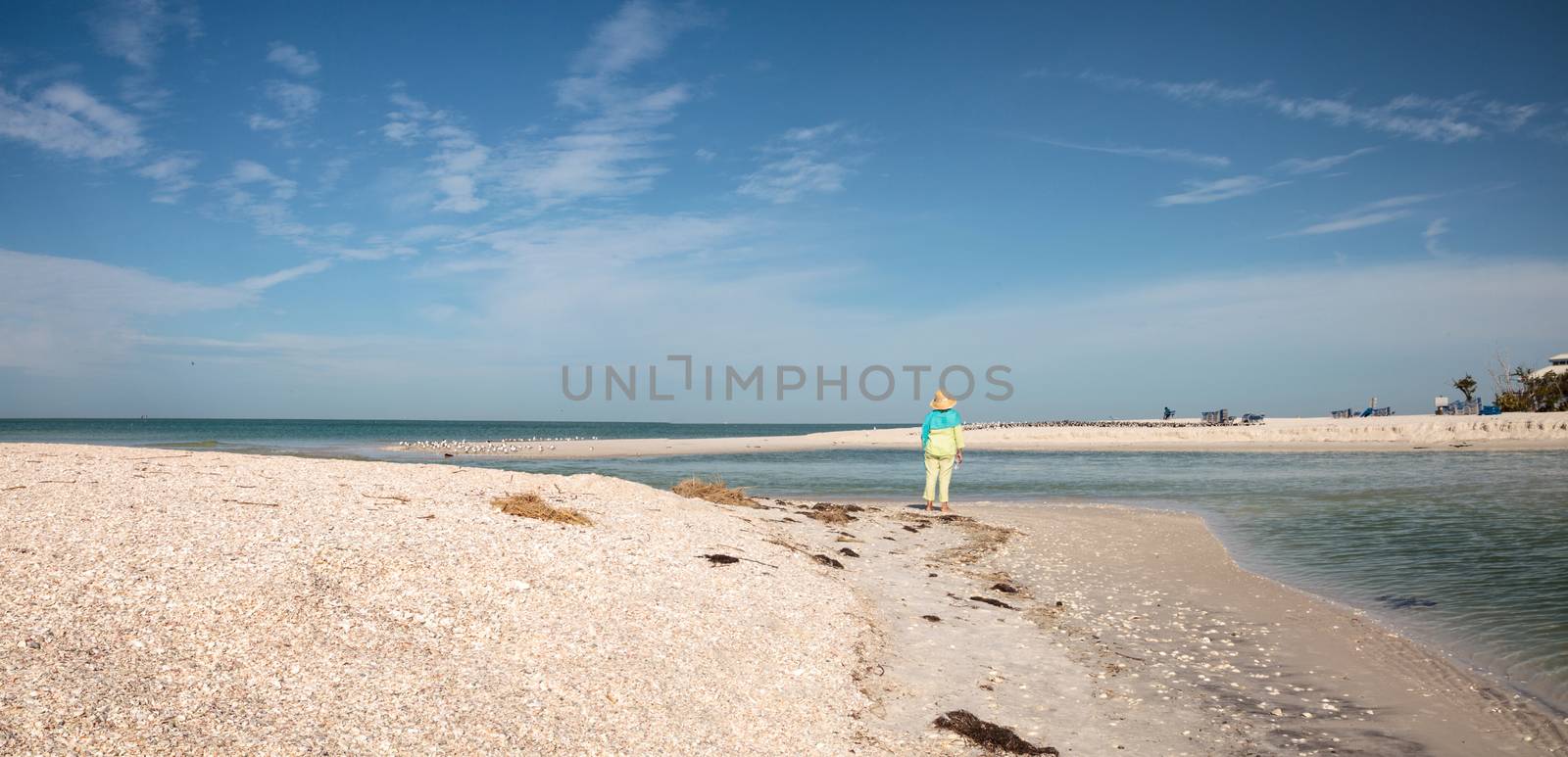 Older woman stands on the white sand beach in front of aqua blue by steffstarr