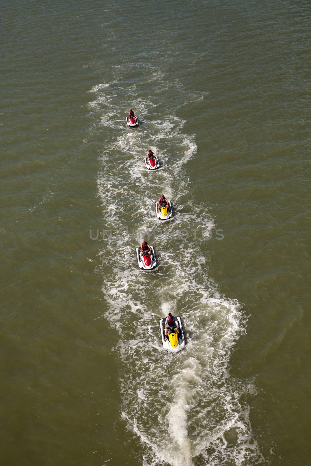 Group of jet skies zip along the ocean in a straight line, making waves in the ocean in the bay in front of Marco Island, Florida