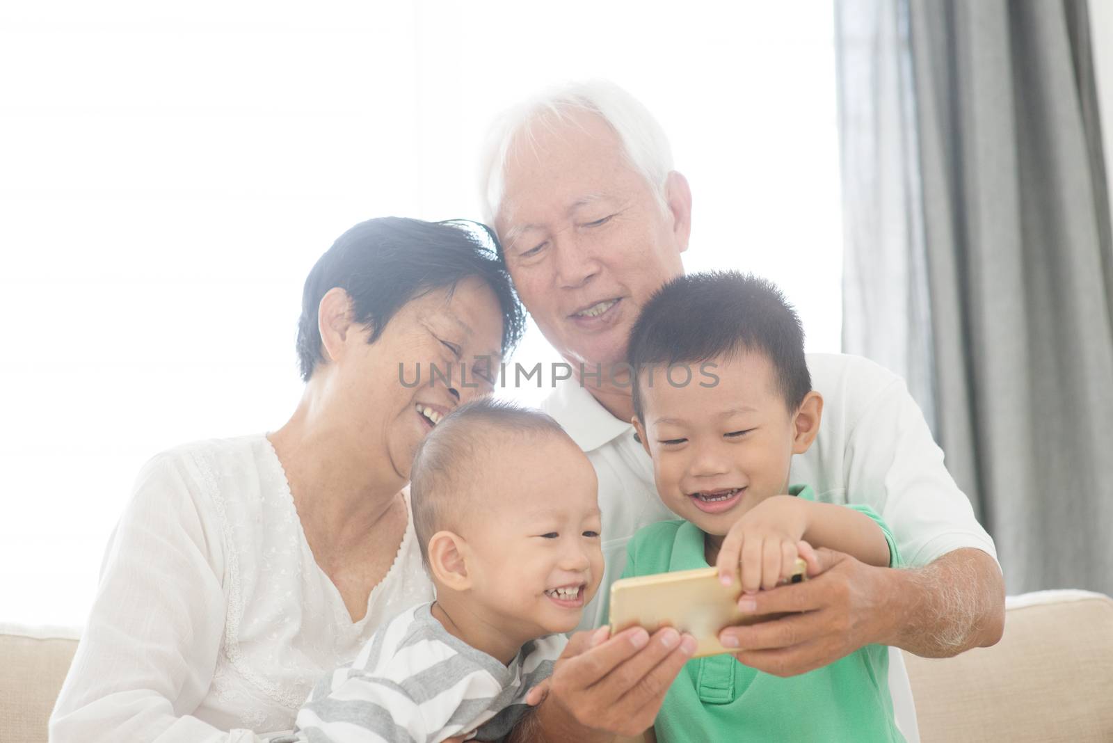Portrait of happy Asian grandparents and grandchildren selfie using smart phone at home, family indoor lifestyle.