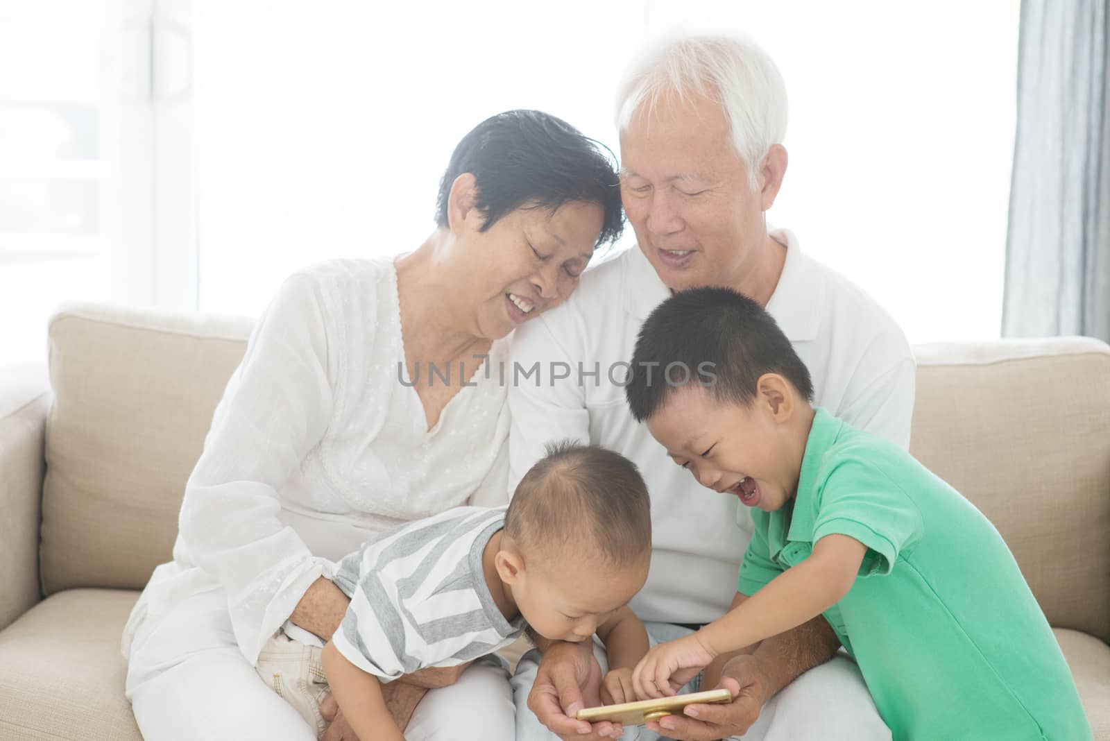 Portrait of happy Asian grandparents and grandchildren using smart phone at home, family indoor lifestyle.